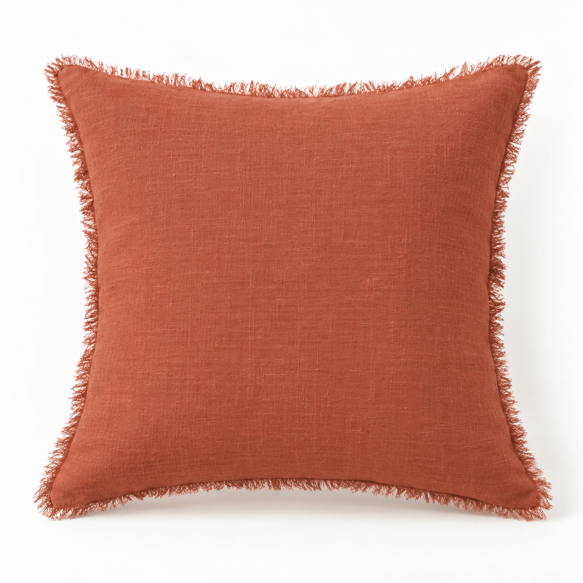 Terracotta raw linen pillow cover with fringe edges on a warm white background